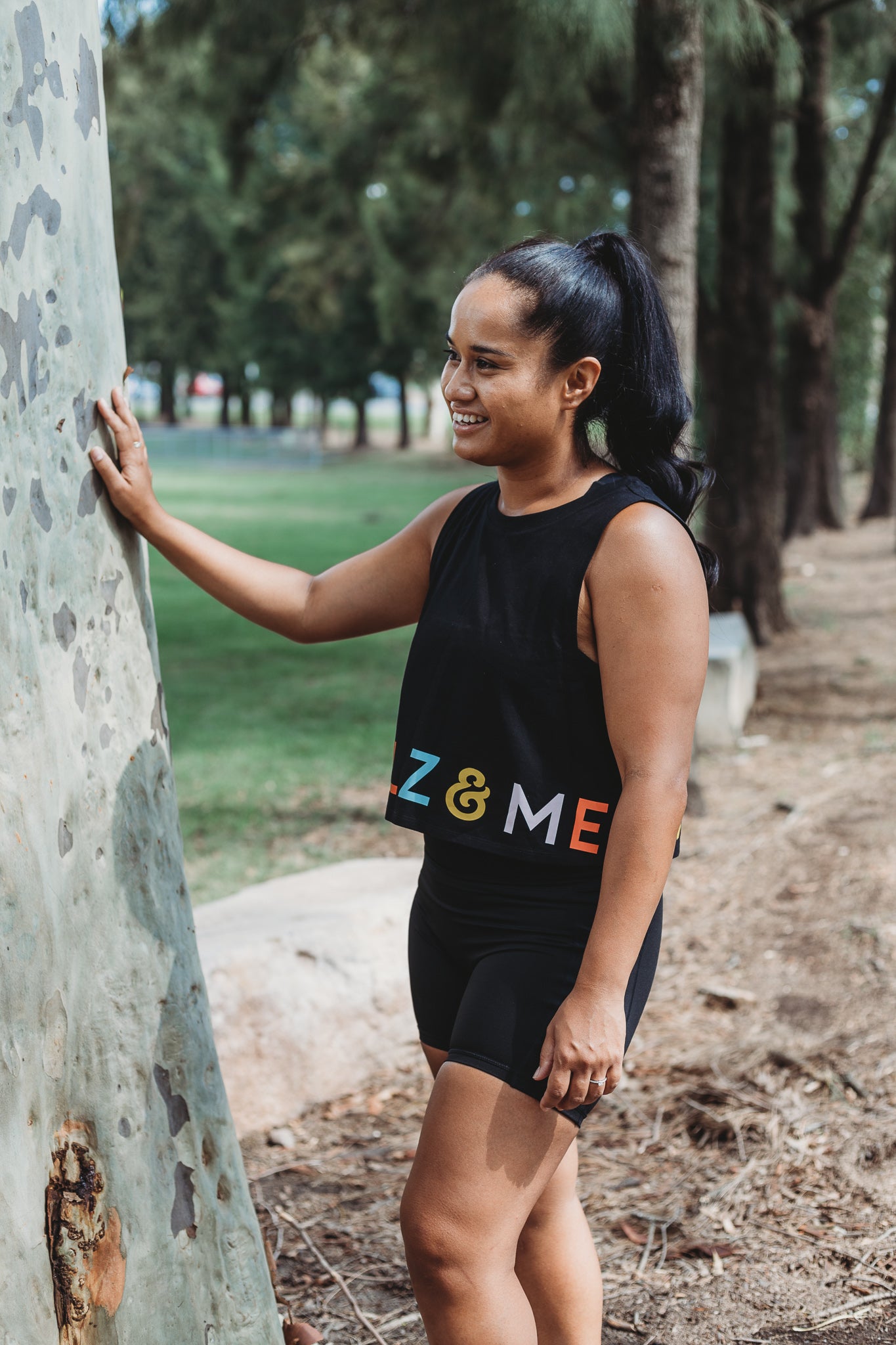 Model wearing the Classic Black Crop Tank Top with the Marlz and Me Logo banding the bottom of the crop. Also wearing the Classic Black Bike Shorts while at a sporting field on a sunny day.