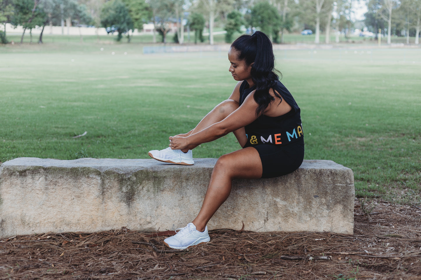 Model wearing the Classic Black Crop Tank Top with the Marlz and Me Logo banding the bottom of the crop. Also wearing the Classic Black Bike Shorts while at a sporting field on a sunny day.