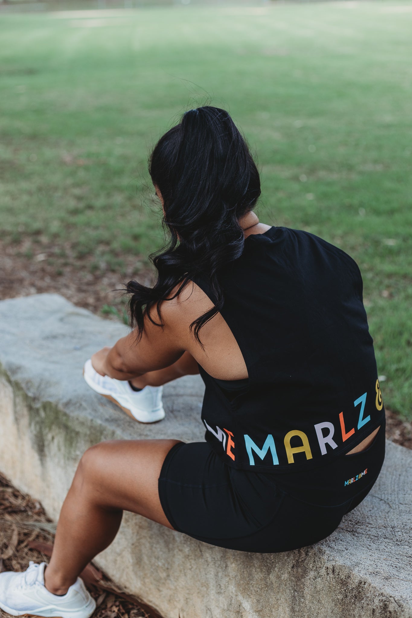 Model wearing the Classic Black Crop Tank Top with the Marlz and Me Logo banding the bottom of the crop. Also wearing the Classic Black Bike Shorts while tying her shoe laces.