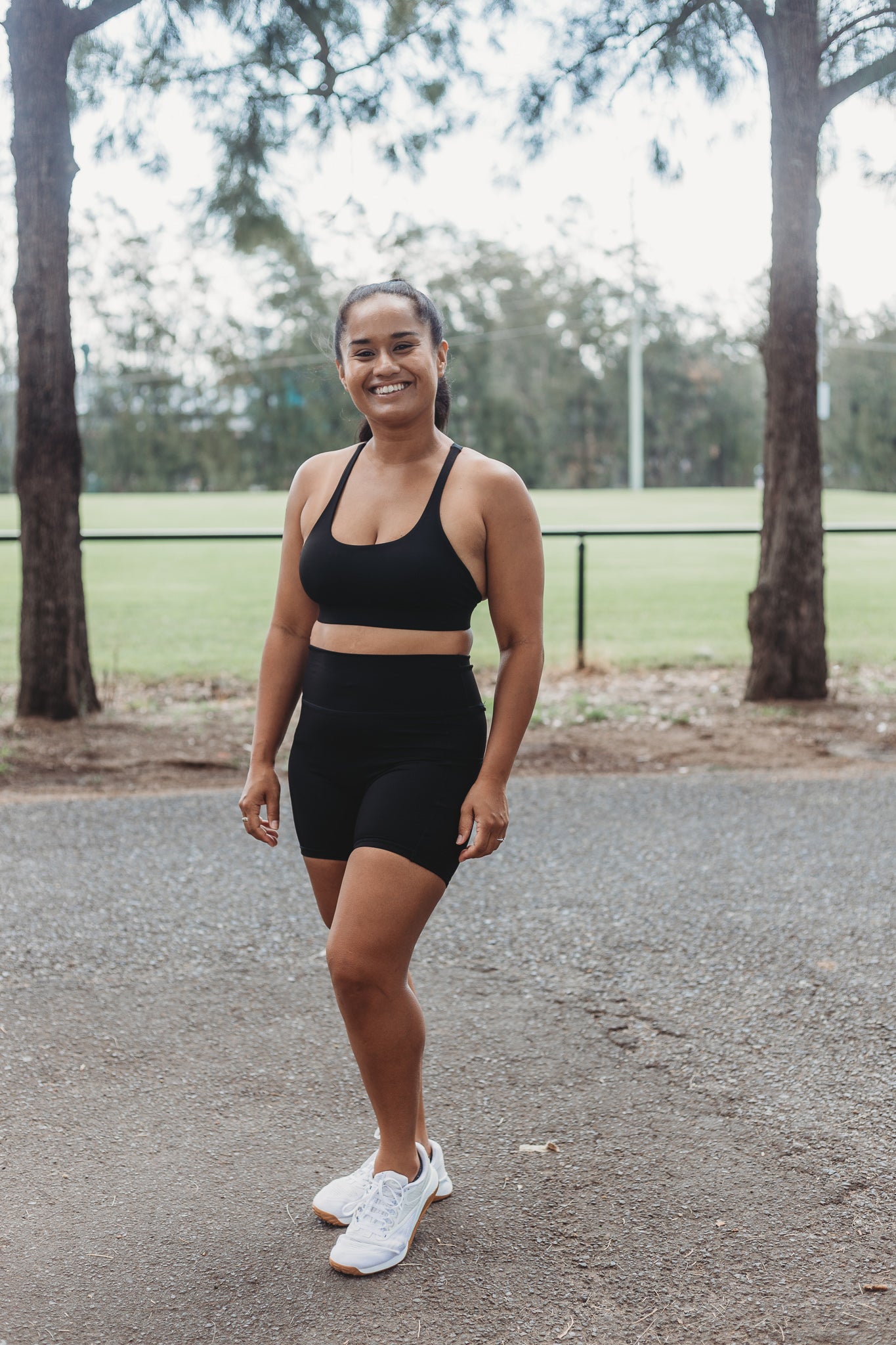 Model wearing Black Sports Bra and Bike Shorts taking a walk at a sporting field in a sunny day.