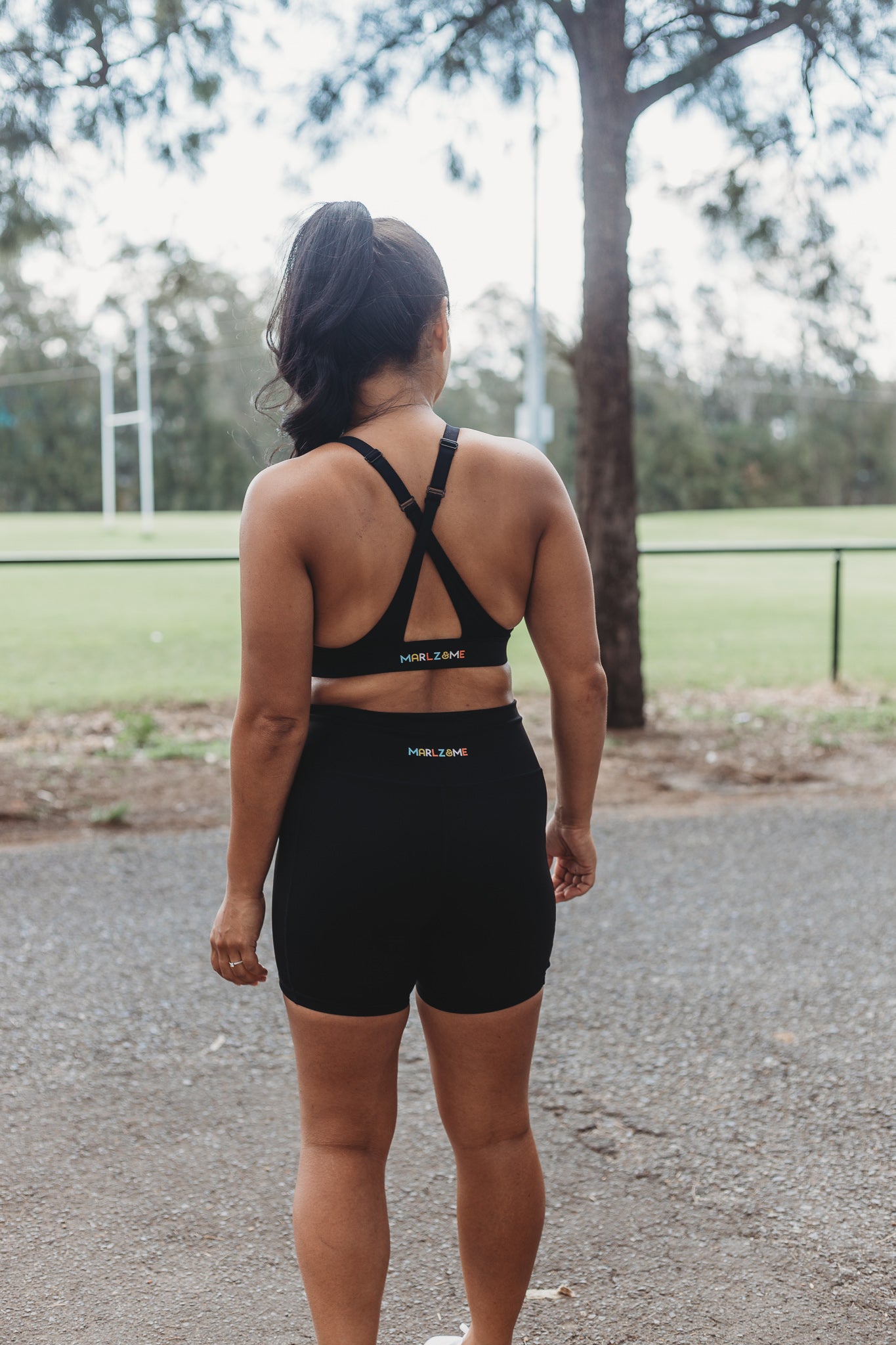 Model wearing Black Sports Bra and Bike Shorts taking a walk at a sporting field in a sunny day.